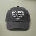 Charcoal grey dad hat embroidered in white with DOUG'S SMALL ENGINE REPAIR above a spark plug.