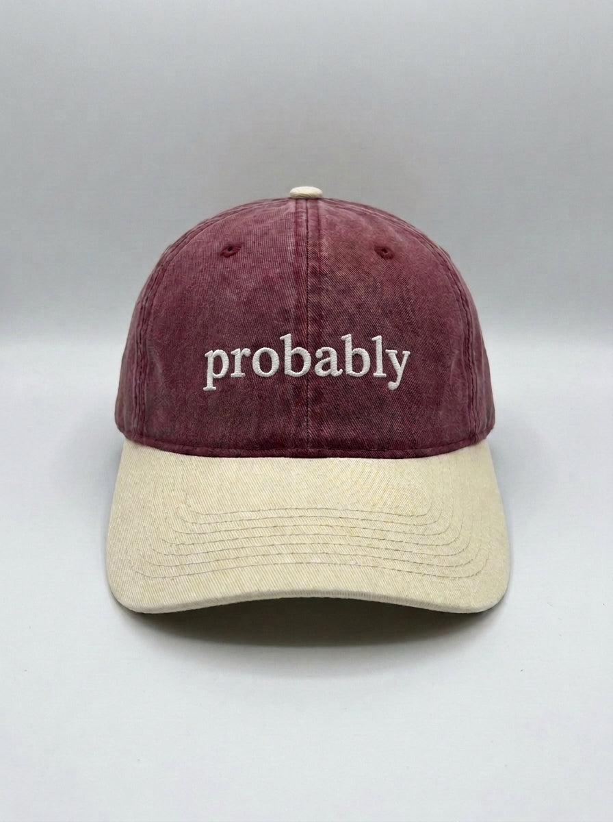 Maroon dad hat with a cream brim, embroidered in white with the lowercase word probably.