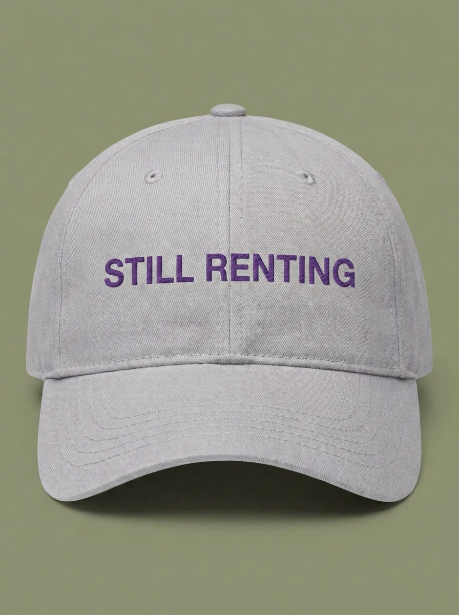 Light grey dad hat embroidered in purple with STILL RENTING.